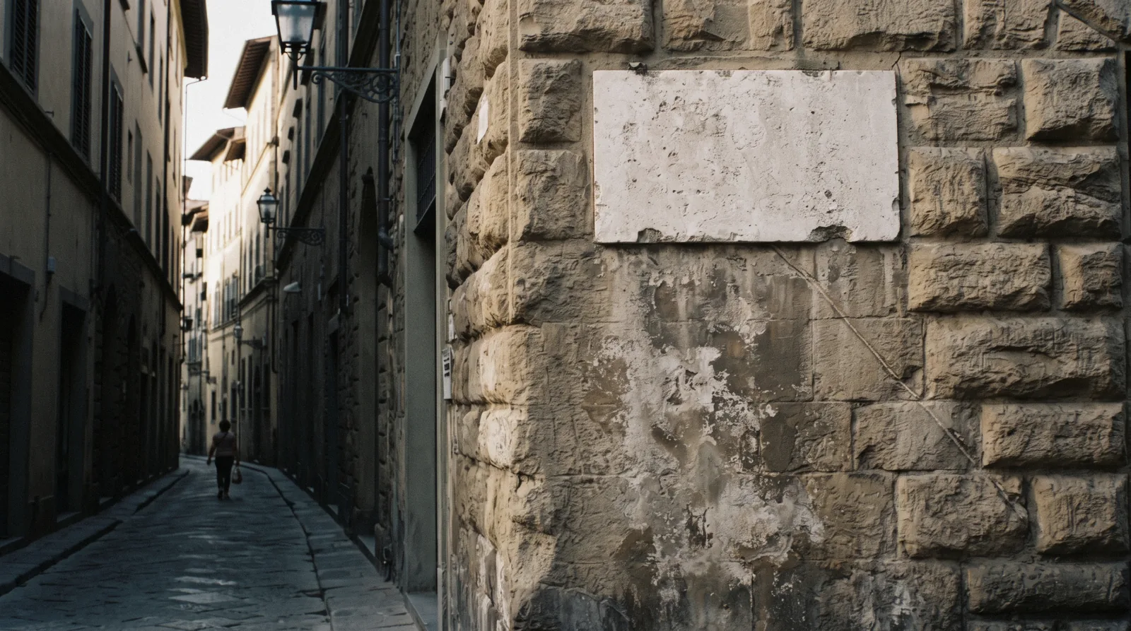 A stone high-water plaque set above head height on a rusticated palazzo wall marking the 1966 flood in Florence, on a narrow shaded street