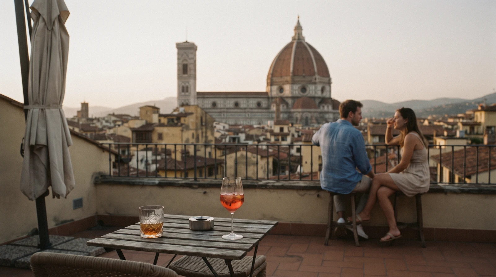 Golden hour from a hotel roof terrace over the Duomo's dome and Giotto's bell tower, the view a rooftop bar in Florence sells