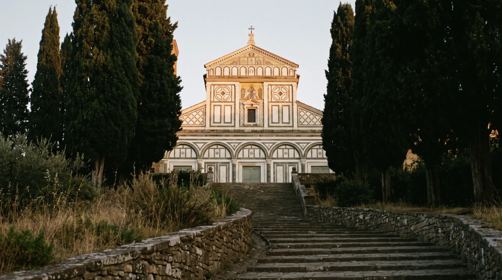 Green and white marble façade of San Miniato al Monte above Florence in late afternoon light with cypresses beside it