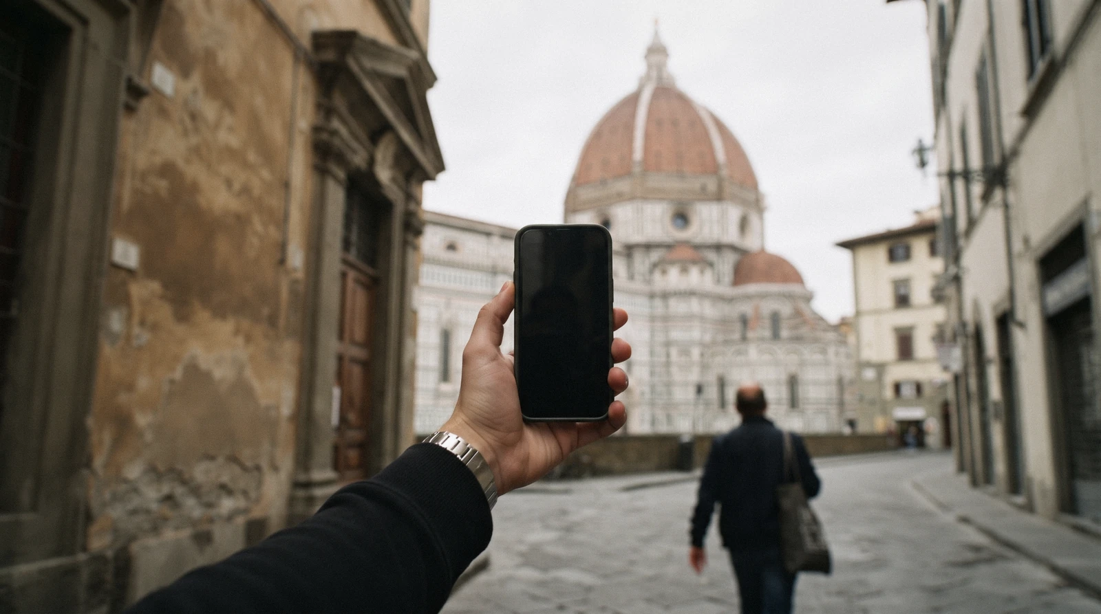 A hand holding a phone showing a map at a street corner in central Florence with the cathedral dome behind, the everyday use of a Florence eSIM and mobile data in Italy