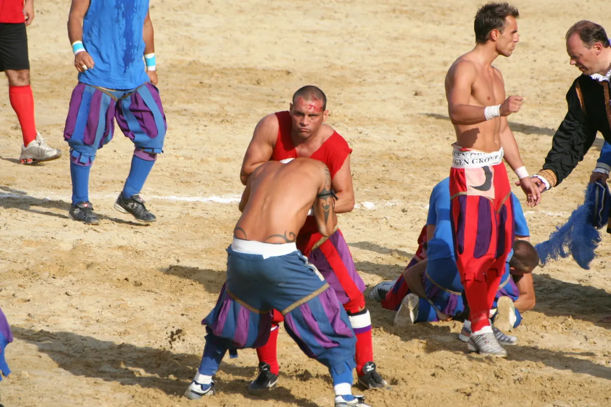 Calcio Storico players in red and blue-purple livery grappling on the sand pitch of Piazza Santa Croce
