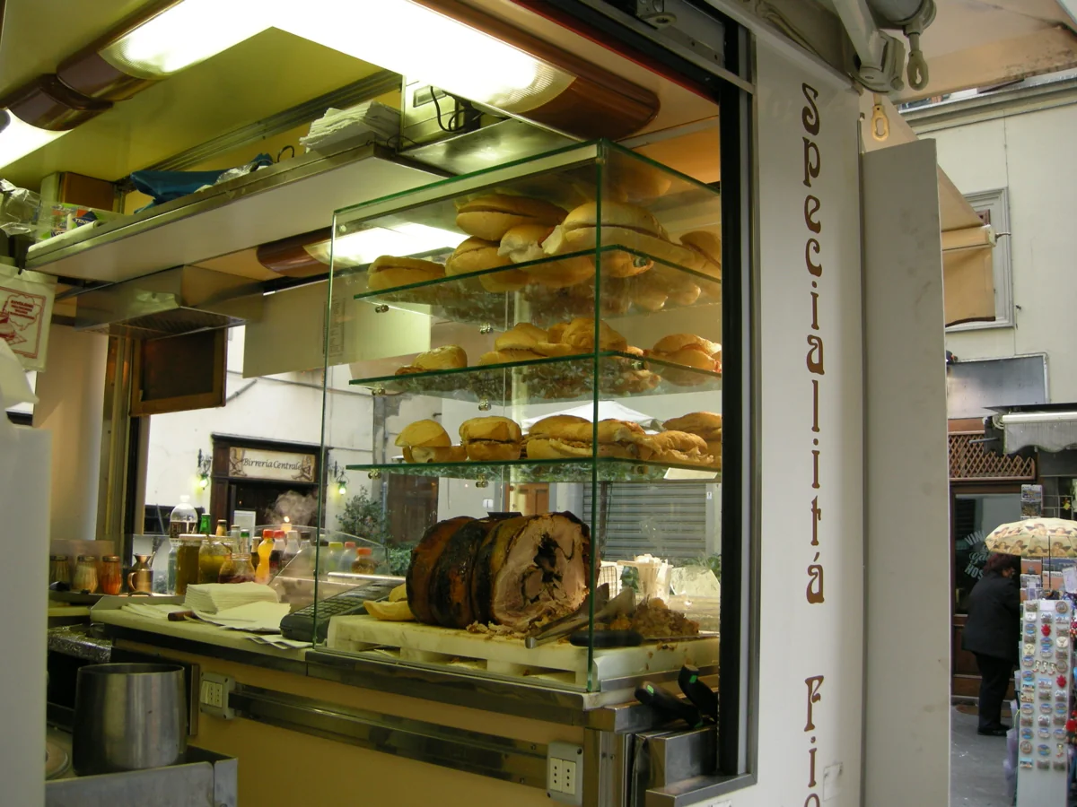 A lampredotto and porchetta kiosk in central Florence, sandwiches stacked behind glass and steam rising from the pot