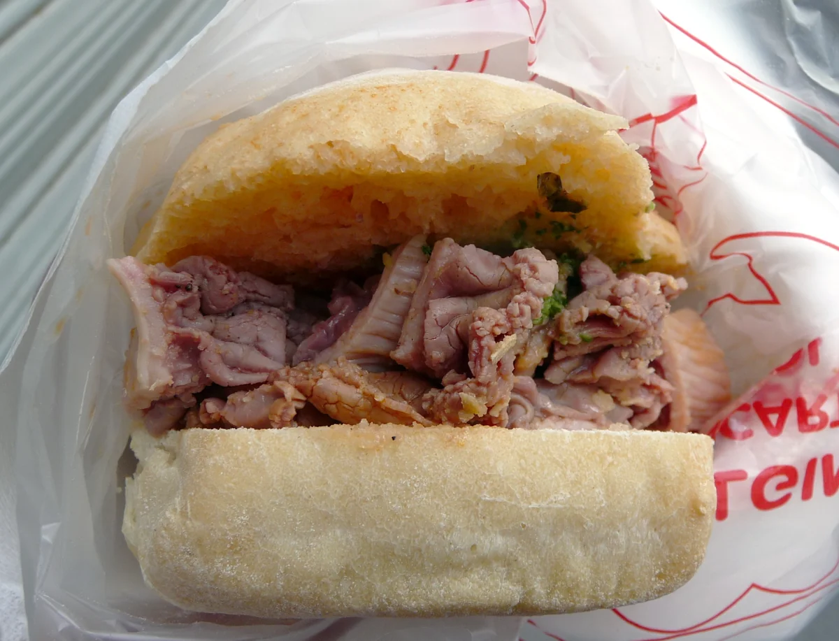 A lampredotto sandwich in its paper wrapper, the boiled tripe piled between halves of a soft roll
