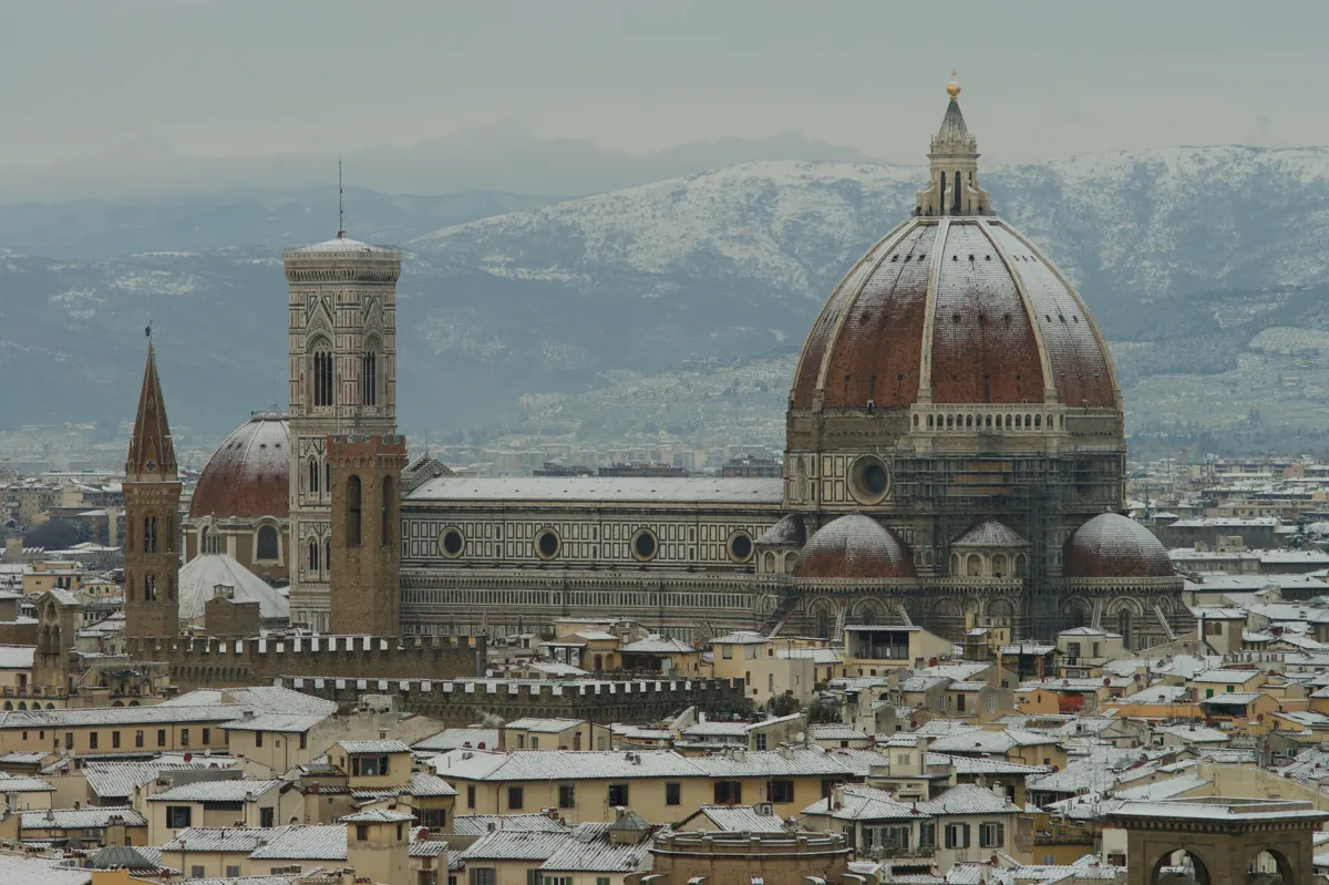 Florence Cathedral and Giotto's bell tower under snow, white rooftops and snowy hills behind