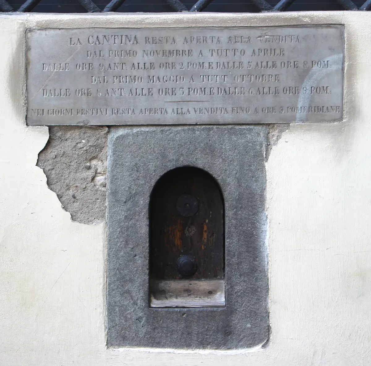 A wine window in Florence with a small wooden door and knockers under a marble plaque of cellar selling hours, Via delle Belle Donne 2